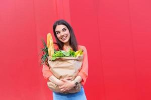 jovem segurando uma sacola de compras cheia de produtos hortícolas, jovem segurando uma sacola de papel de mercearia cheia de vegetais frescos. mulher segurando uma sacola de compras cheia de alimentos frescos foto