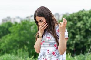 conceito de doença de primavera. jovem fêmea segurando guardanapos e spray para alergia ou febre, nariz escorrendo e resfriado no jardim florido. mulher irritada com alergia sazonal foto