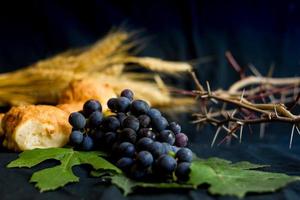 pão de uvas de trigo e coroa de espinhos em fundo preto como um símbolo do cristianismo foto