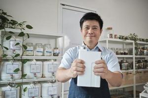 retrato do lojista masculino tailandês sorri e olha para a câmera com recipiente reutilizável, produtos orgânicos na loja de recarga, mercearia com desperdício zero e negócios sustentáveis e ecológicos sem plástico. foto