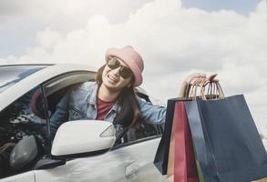 mulher asiática tailandesa, garota feliz segurando a sacola de compras e mostrando no carro foto