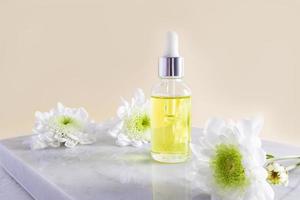 produto cosmético orgânico natural em um frasco de vidro com um conta-gotas em um ladrilho de mármore branco com flores. fundo bege. autocuidados. foto