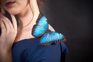 close-up de uma borboleta azul no ombro de uma jovem em um fundo escuro. o conceito de fragilidade da natureza foto