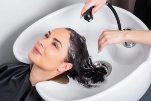 cabeleireiro profissional lavando cabelo de jovem no salão de beleza foto