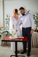 noivos alegremente cortam e provam o bolo de casamento foto