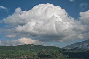 vista panorâmica das montanhas com pinheiros e nuvens fofas brancas, tiro panorâmico das montanhas ao meio-dia na costa do mar Egeu foto