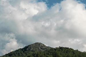 vista panorâmica da montanha com parapentes voando em alta altitude e nuvens fofas brancas, tiro panorâmico de montanhas ao meio-dia na costa do mar Egeu foto