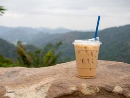 um copo de café gelado é colocado sobre uma rocha contra um fundo de montanhas e céu. foto
