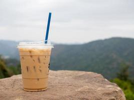 um copo de café gelado é colocado sobre uma rocha contra um fundo de montanhas e céu. foto