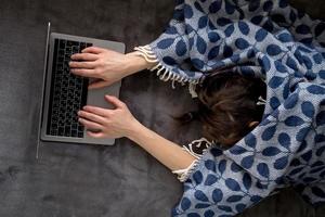 uma mulher coberta com uma manta adormeceu trabalhando com um laptop, deitada em um sofá macio em casa. foto