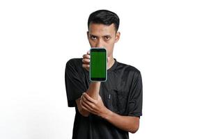 homem asiático animado vestindo camiseta preta de treino, apontando para a tela verde do smartphone. isolado por fundo branco foto