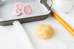 preparação de massa para fazer biscoitos com moldes em forma de flores, um rolo e uma assadeira, conceito de cozimento de alimentos em casa. foto