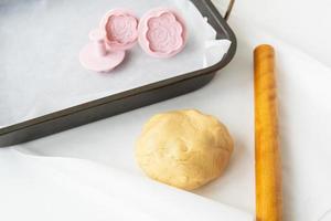 preparação de massa para fazer biscoitos com moldes em forma de flores, um rolo e uma assadeira, conceito de cozimento de alimentos em casa. foto