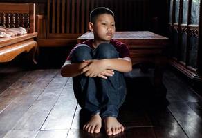 retrato de um menino asiático, cara triste de criança, criança infeliz sentada abraçando os joelhos no chão, emoção triste e rosto triste, conceito de depressão infantil foto
