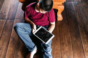 retrato de um menino asiático, cara triste de criança, criança infeliz sentada segurando computador tablet quebrado, emoção triste e rosto triste, conceito de crianças deprimidas foto