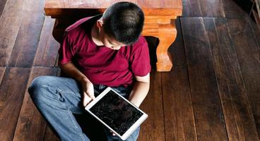 retrato de um menino asiático, cara triste de criança, criança infeliz sentada segurando computador tablet quebrado, emoção triste e rosto triste, conceito de crianças deprimidas foto