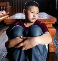 retrato de um menino asiático, cara triste de criança, criança infeliz sentada abraçando os joelhos no chão, emoção triste e rosto triste, conceito de depressão infantil foto