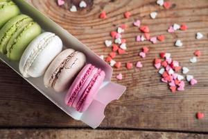 macarons variados em uma caixa polvilhada com pequenos corações em um fundo de madeira, vista superior foto