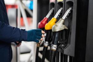 feche a mão do homem segure a bomba de combustível enquanto reabastece seu carro no posto de gasolina em tempo frio. foto