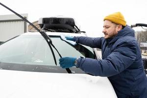 homem limpa o pára-brisa do carro suv americano com um pano de microfibra após a lavagem em clima frio. foto