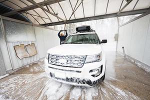 homem lavando carro suv americano de água de alta pressão com rack de teto na lavagem de autoatendimento em clima frio. foto