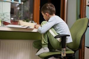 garoto estudando em casa e fazendo lição de casa, educação a distância, sentado à mesa. foto