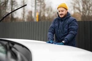 homem limpa o capô do carro suv americano com um pano de microfibra após a lavagem em clima frio. foto