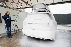 homem lavando carro suv americano com rack de teto em uma lavagem self-service em clima frio. foto