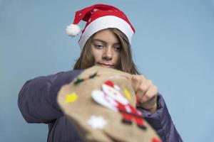 uma garota bonita tira presentes de natal de sua bolsa, uma garota com roupas de inverno em um fundo azul foto