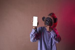 homem asiático vestindo camisa longa azul com máscara de macaco mostrando telefone, foto