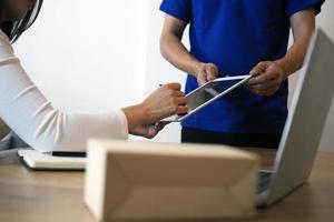 a garota compradora assina no tablet para receber a caixa do pacote do entregador. serviço de entrega rápida foto