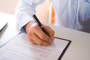 um homem de negócios sentado em um contrato de assinatura de mesa com ênfase na assinatura. foto