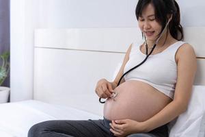 mulher grávida usa um estetoscópio para ouvir o coração do bebê. ouvir as vozes do nascituro cria uma relação entre a mãe e o nascituro. felicidade do conceito de grávida. foto