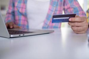 mulher segurando um cartão de crédito para pagar mercadorias por meio de um aplicativo em um laptop. compras online e pagamento no internet banking com cartão de crédito. compras online no conceito de casa foto