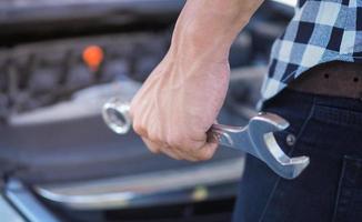 um homem com uma chave na mão para consertar o carro foto