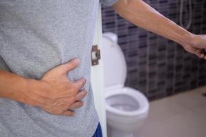 os homens têm dor de estômago e usam as mãos para segurar o estômago no banheiro. constipação ou câncer de cólon foto