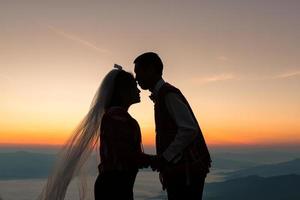 silhueta de casal de noivos apaixonados beijando e segurando a mão juntos durante o nascer do sol com o fundo do céu da manhã foto