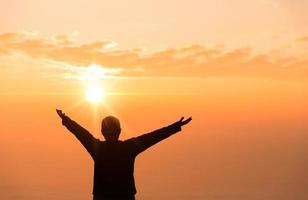 fé do conceito cristão. a oração espiritual entrega o brilho do sol com um belo fundo desfocado do pôr do sol. mãos femininas adoram a Deus com amor e fé. silhueta de uma mulher rezando com uma cruz. foto