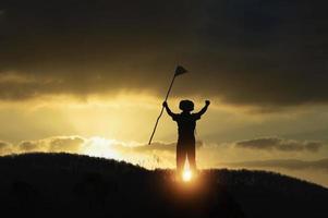 silhueta de escoteiros da américa segurando a bandeira no topo da montanha com céu azul e luz solar. simboliza a liderança dos escoteiros no trekking que atinge suas metas e objetivos. foto