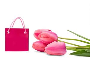 tulipas cor de rosa com folhas verdes e sacola de compras estão sobre fundo branco isolado. feriados, mulheres internacionais, dia das mães, aniversário, 8 de março, venda. copie o espaço foto