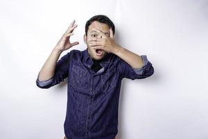 homem asiático espreitando óbvio engraçado na camisa azul isolada no fundo branco. foto