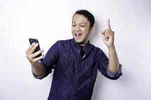 um retrato de um homem asiático feliz vestindo uma camisa azul e segurando seu telefone, isolado por fundo branco foto
