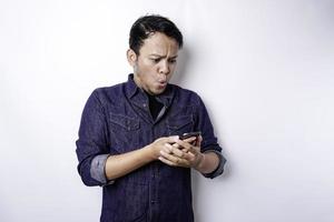 homem asiático chocado vestindo camisa azul e segurando seu telefone, isolado por fundo branco foto