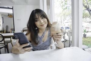 uma mulher asiática feliz sorrindo em um restaurante, vestindo uma blusa e segurando seu telefone foto