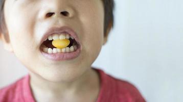 garotinho mordendo um doce amarelo na boca conceito de saúde bucal foto