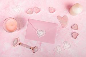 raspagem de pedra de quartzo rosa natural guasha e massageador de rolo para rosto, envelope, velas em rosa. foto