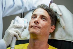 homem bonito closeup tendo terapia de luz colorida para estimular a pele facial pelo bem-estar cosmetologista profissional. foto