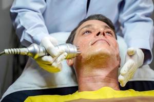 homem bonito closeup tendo terapia para estimular a pele facial e tratamento facial ultra-sônico pelo bem-estar cosmetologista profissional. foto