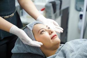 closeup enfermeira de beleza mostra creme esfoliante facial nas mãos antes de fazer massagem facial com esfoliação facial orgânica no rosto do cliente. foto