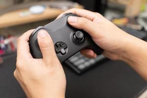 controlador de jogo preto com a mão. as mãos do homem seguram o controlador do console em primeiro plano. jogando videogame em casa. foto